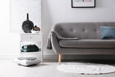 Photo of Living room interior with vases on side table and comfortable sofa near white wall