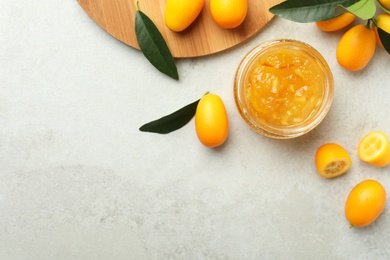 Delicious kumquat jam in jar and fresh fruits on light grey table, flat lay. Space for text