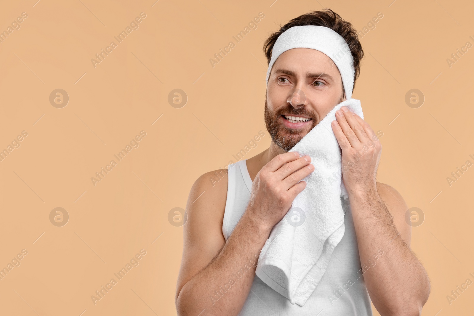 Photo of Washing face. Man with headband and towel on beige background, space for text