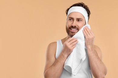 Washing face. Man with headband and towel on beige background, space for text