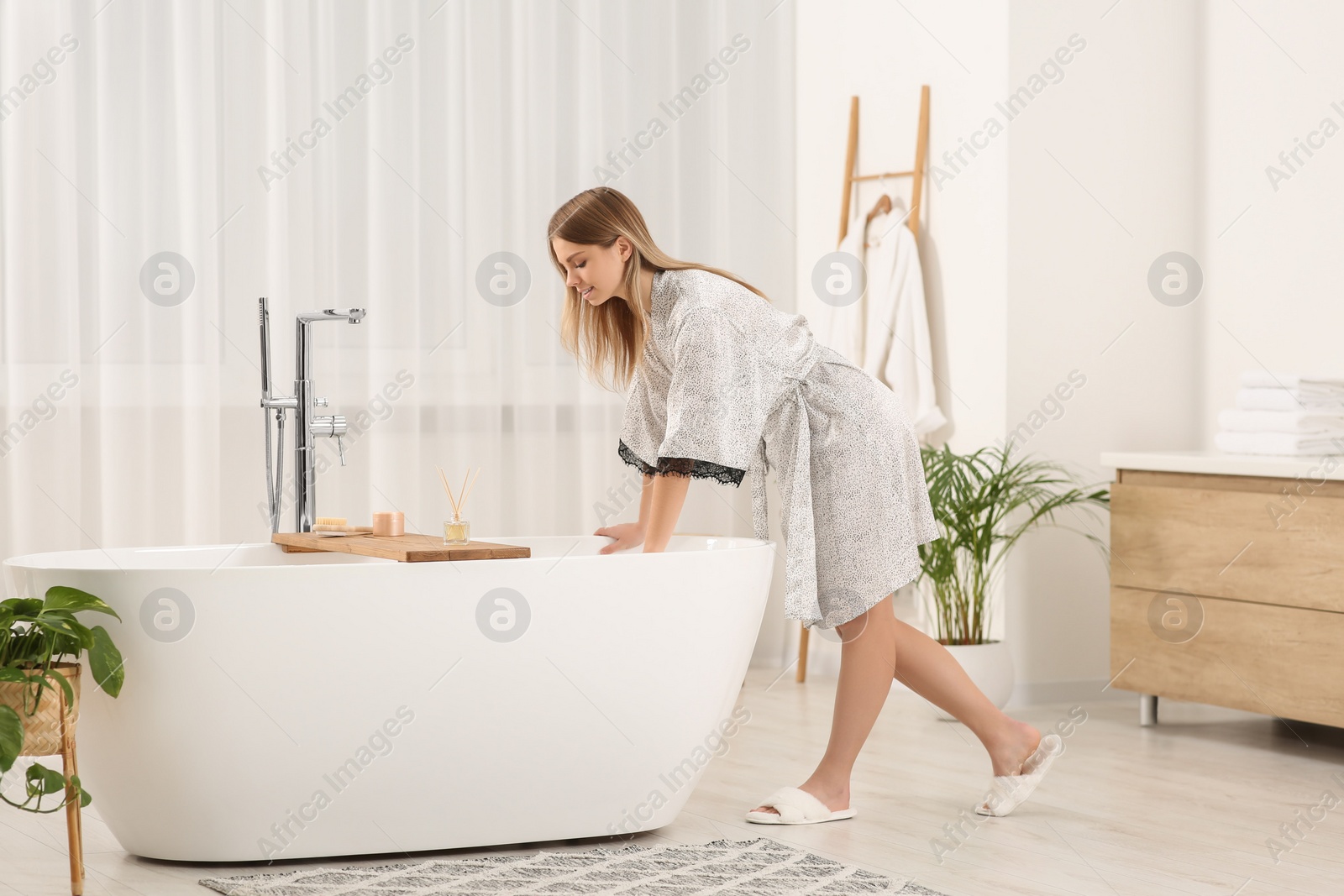 Photo of Beautiful woman wearing stylish robe near tub in bathroom