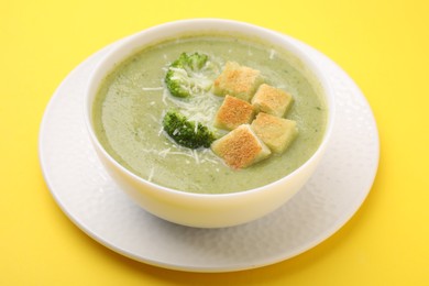 Photo of Delicious broccoli cream soup with croutons and cheese on yellow background, closeup