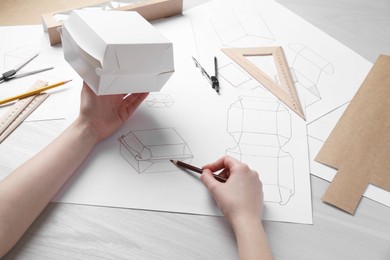 Woman creating packaging design at light wooden table, closeup