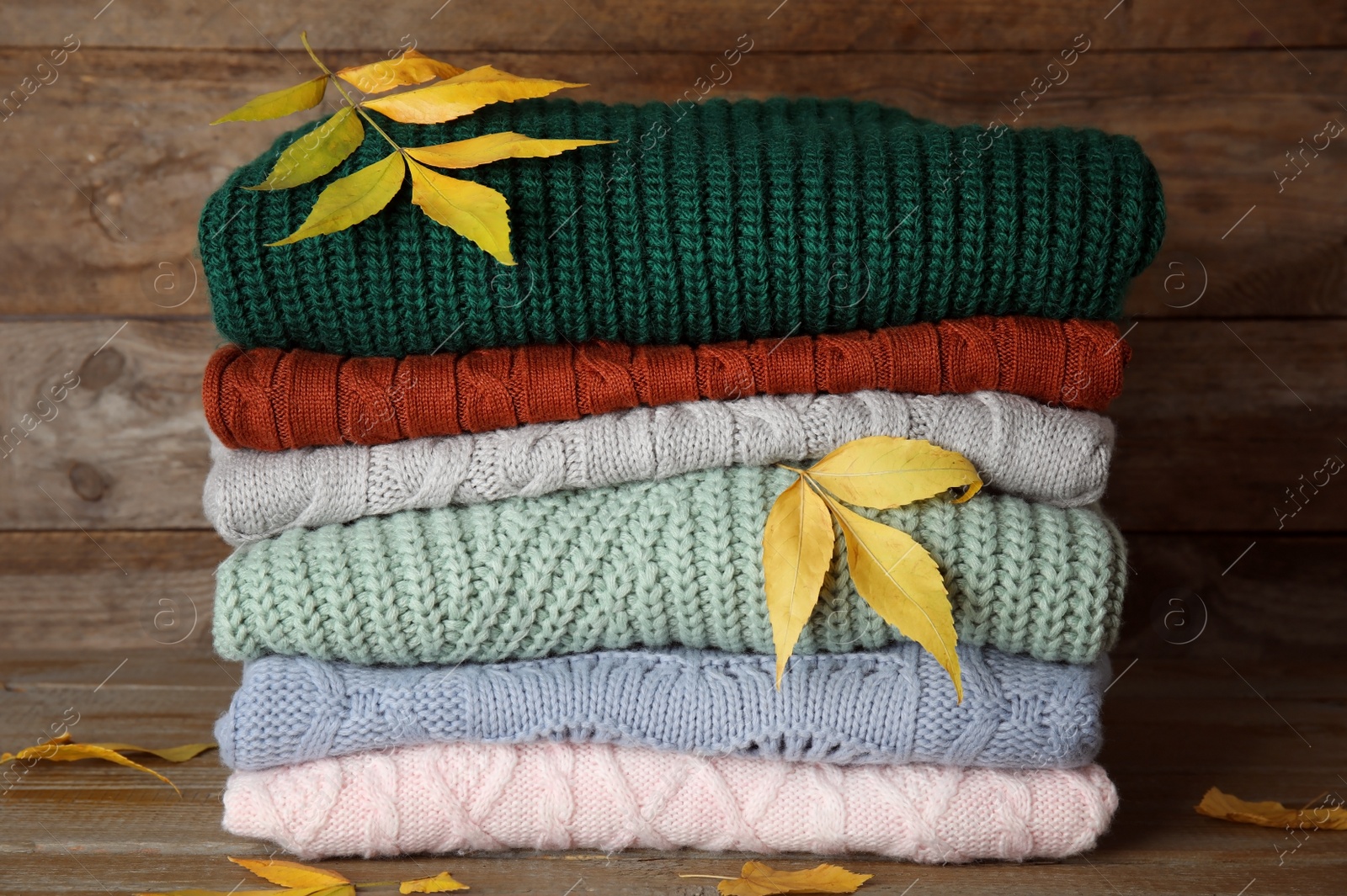 Photo of Stack of warm knitted clothes and autumn leaves on wooden background