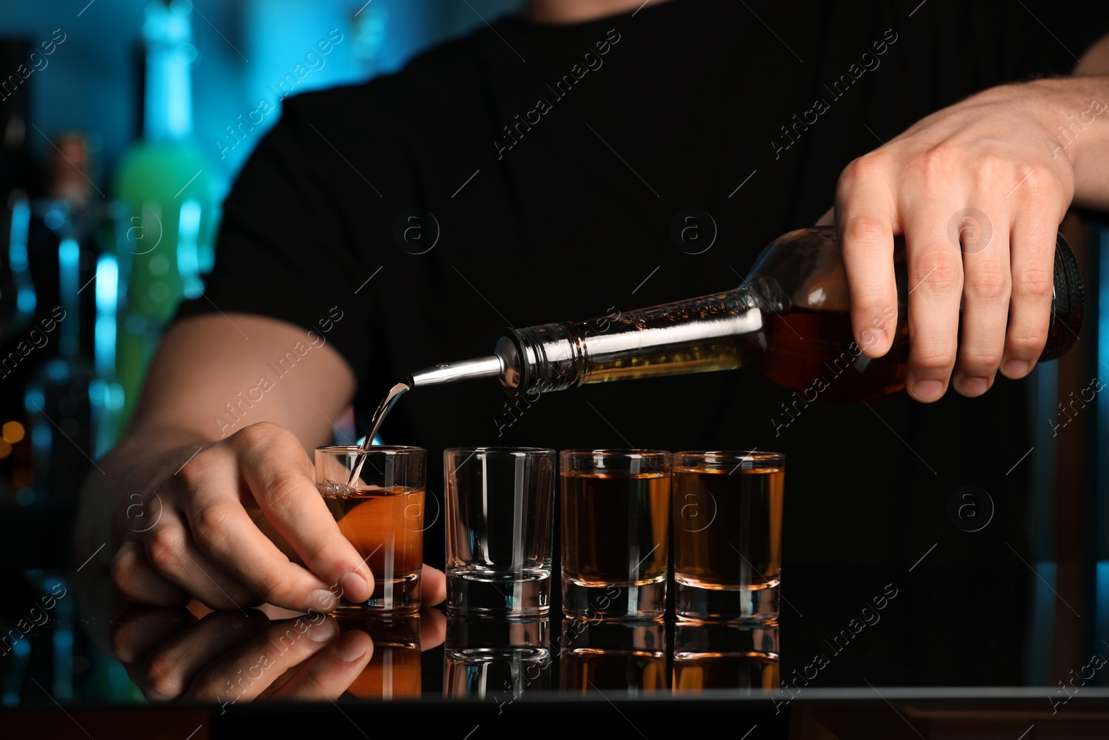 Photo of Bartender pouring alcohol drink into shot glass at mirror counter in bar, closeup