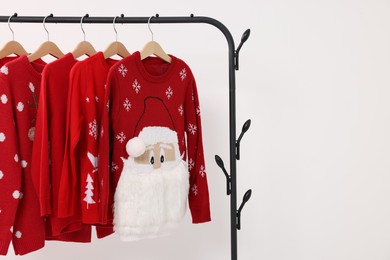 Rack with different Christmas sweaters on white background, space for text