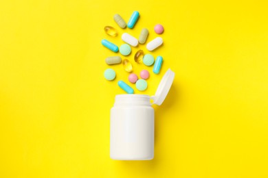 Different vitamin pills and bottle on yellow background, top view.