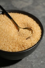 Photo of Brown sugar in bowl and spoon on grey textured table, closeup