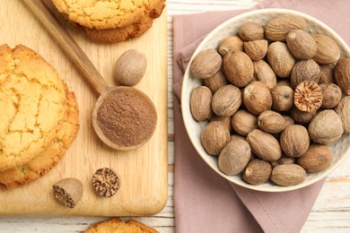 Nutmeg powder, seeds and tasty cookies on white wooden table, flat lay