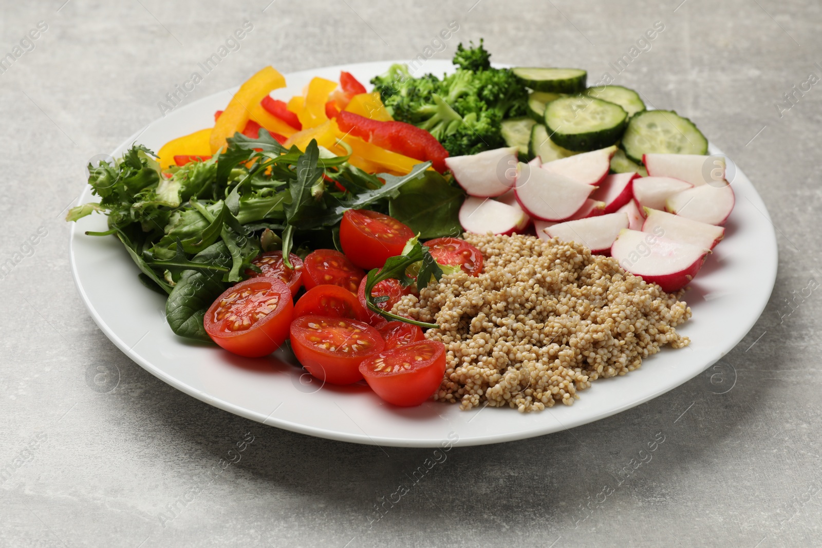 Photo of Vegetarian diet. Plate with tasty vegetables and quinoa on light grey table