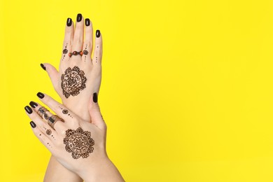 Photo of Woman with henna tattoos on hands against yellow background, closeup and space for text. Traditional mehndi ornament