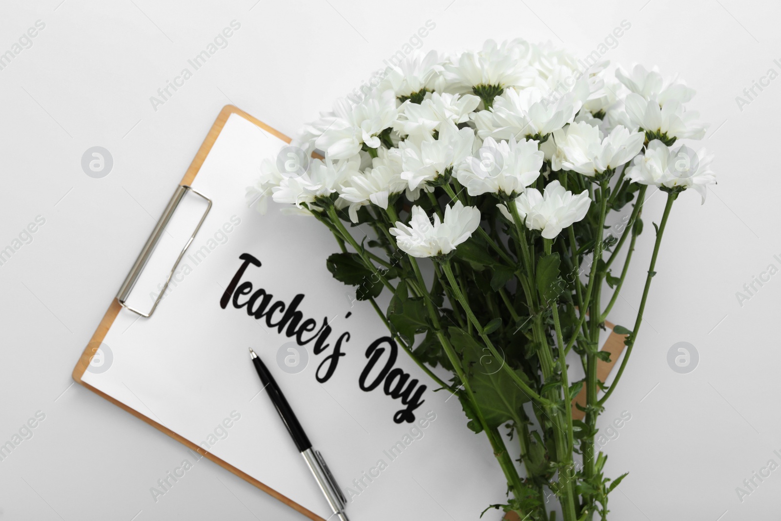 Photo of Beautiful flowers and clipboard with words TEACHER'S DAY on white background, top view