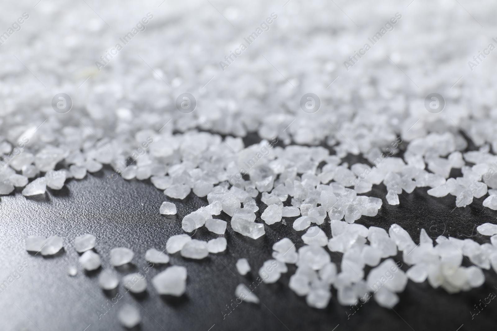 Photo of Scattered white natural salt on black table, closeup