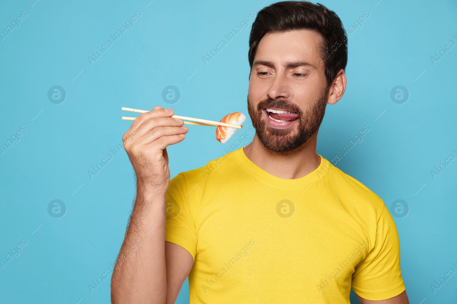 Photo of Emotional man holding tasty sushi with chopsticks on light blue background