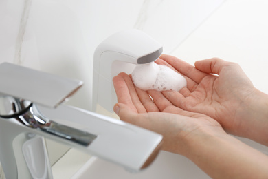 Woman using automatic soap dispenser in bathroom, closeup