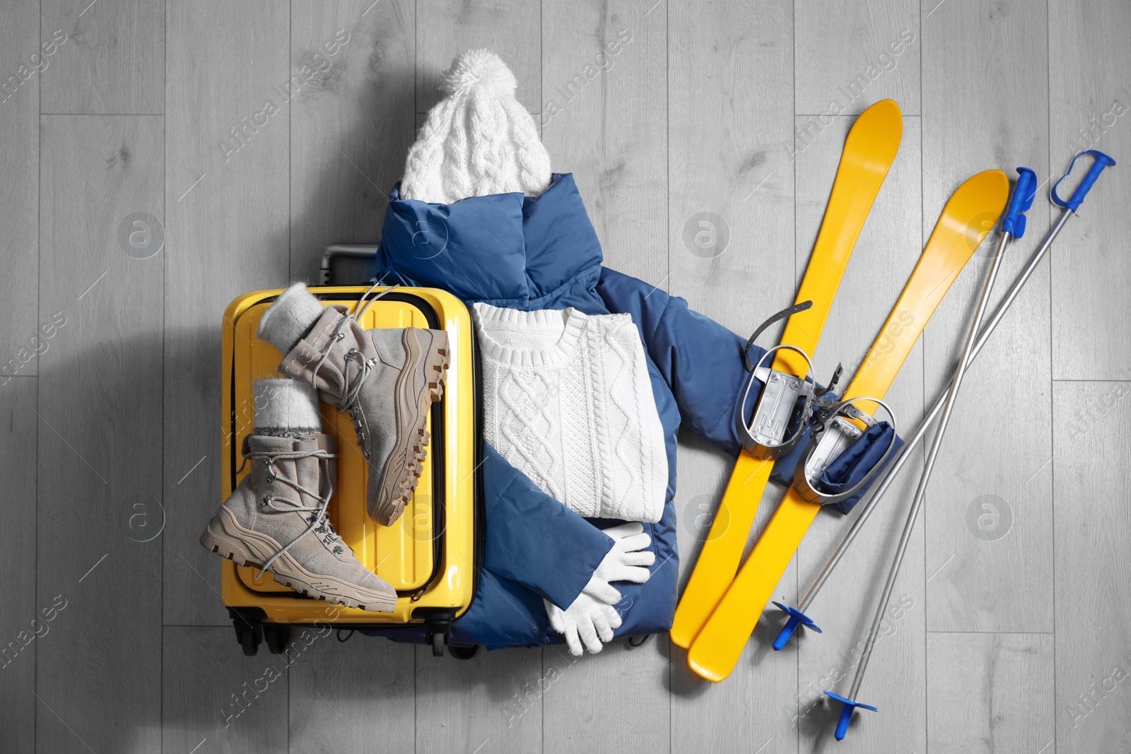 Photo of Suitcase with warm clothes and skis on wooden floor, flat lay. Winter vacation