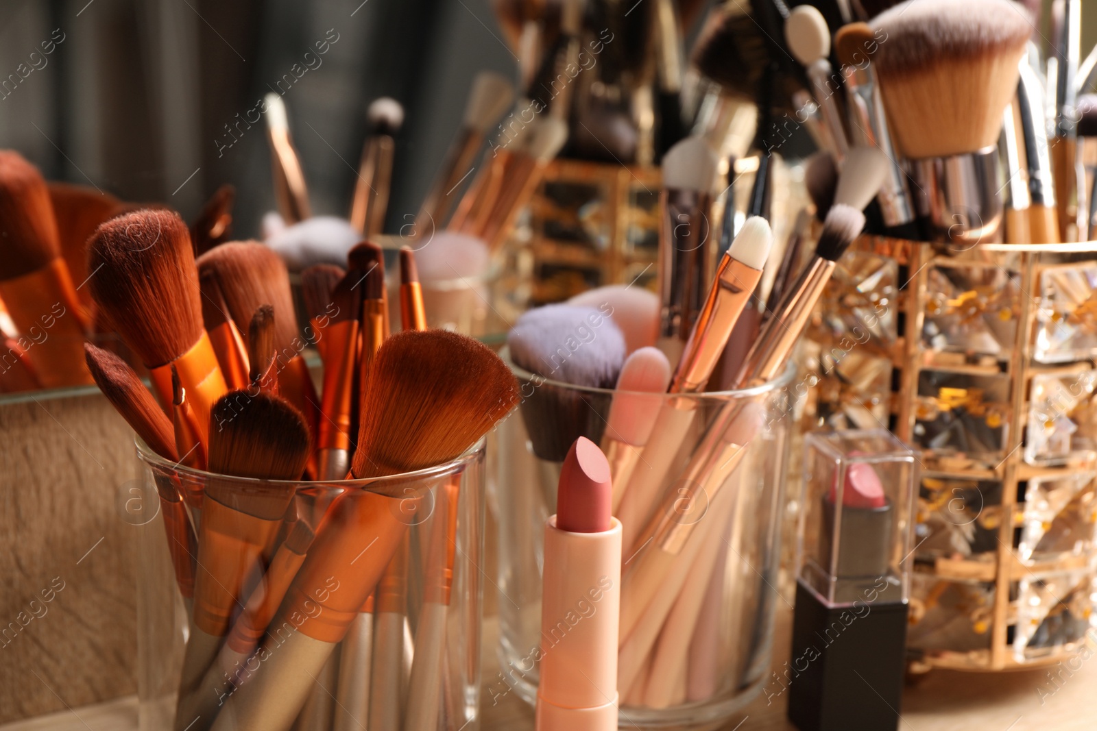 Photo of Set of professional brushes and makeup products near mirror on wooden table, closeup