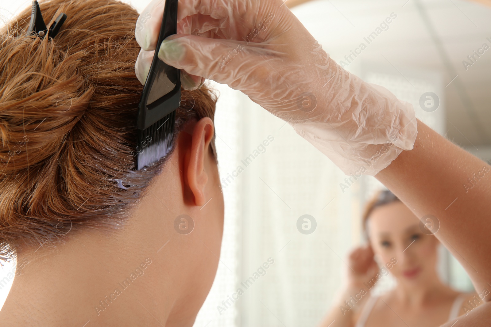 Photo of Young woman applying hair dye on roots in front of mirror at home, closeup