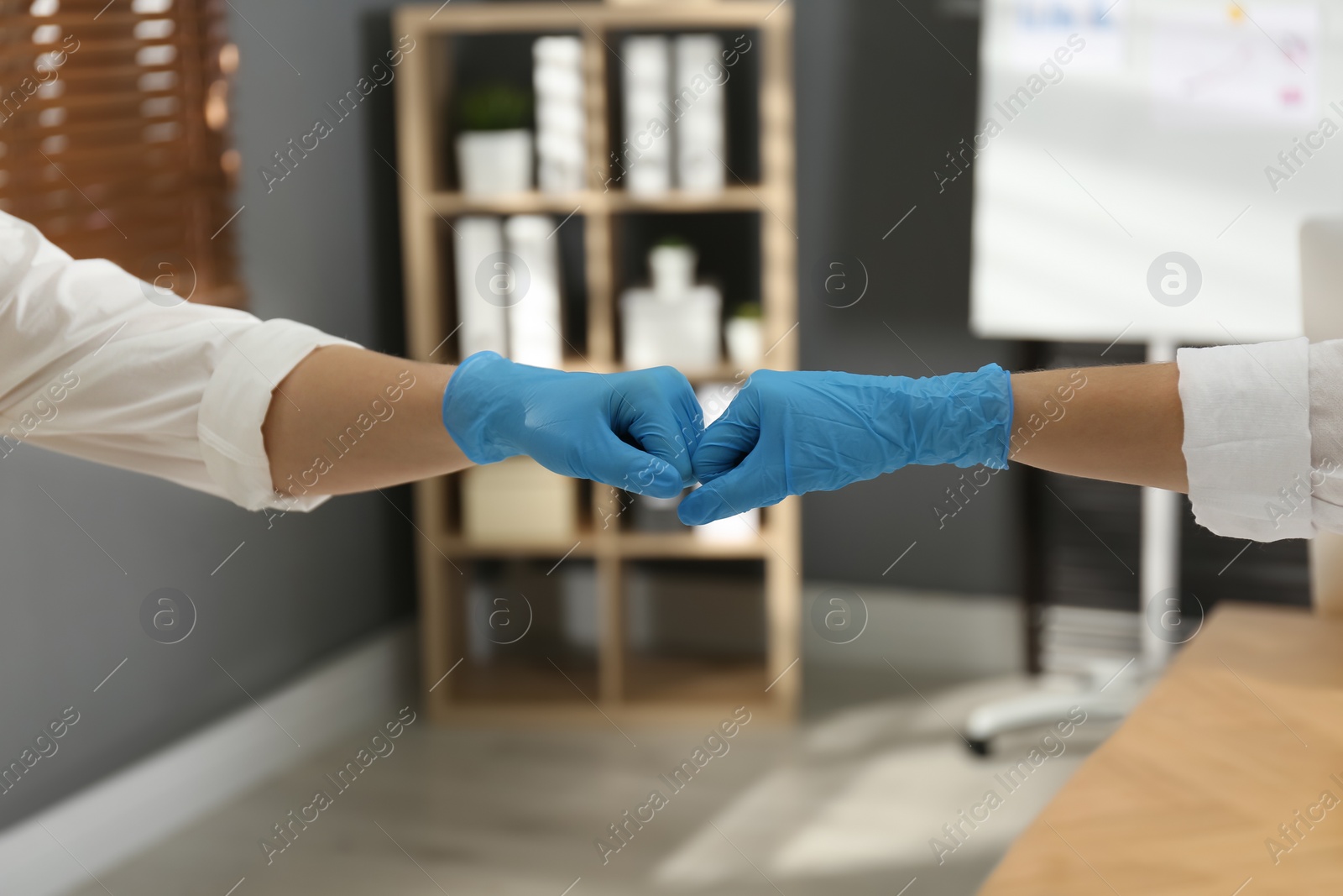 Photo of People greeting each other by bumping fists instead of handshake indoors, closeup