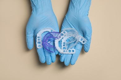 Photo of Bite correction. Dentist in medical gloves holding different mouth guards on beige background, top view
