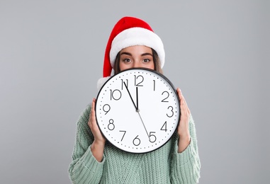 Woman in Santa hat with clock on grey background. New Year countdown