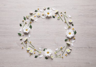 Wreath made of chamomile flowers and green leaves on white wooden background, flat lay. Space for text