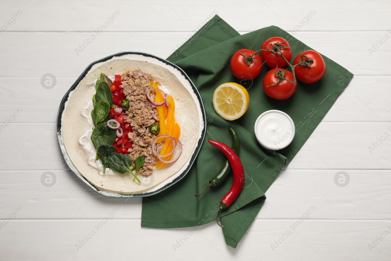 Photo of Delicious tortilla with tuna and vegetables on white wooden table, flat lay. Cooking shawarma