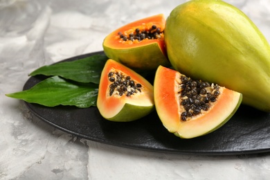 Fresh ripe papaya fruits with green leaves on grey table