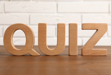 Photo of Word Quiz made with wooden letters on table near white brick wall