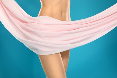 Slim young woman covered with silk fabric on color background, closeup. Fit body