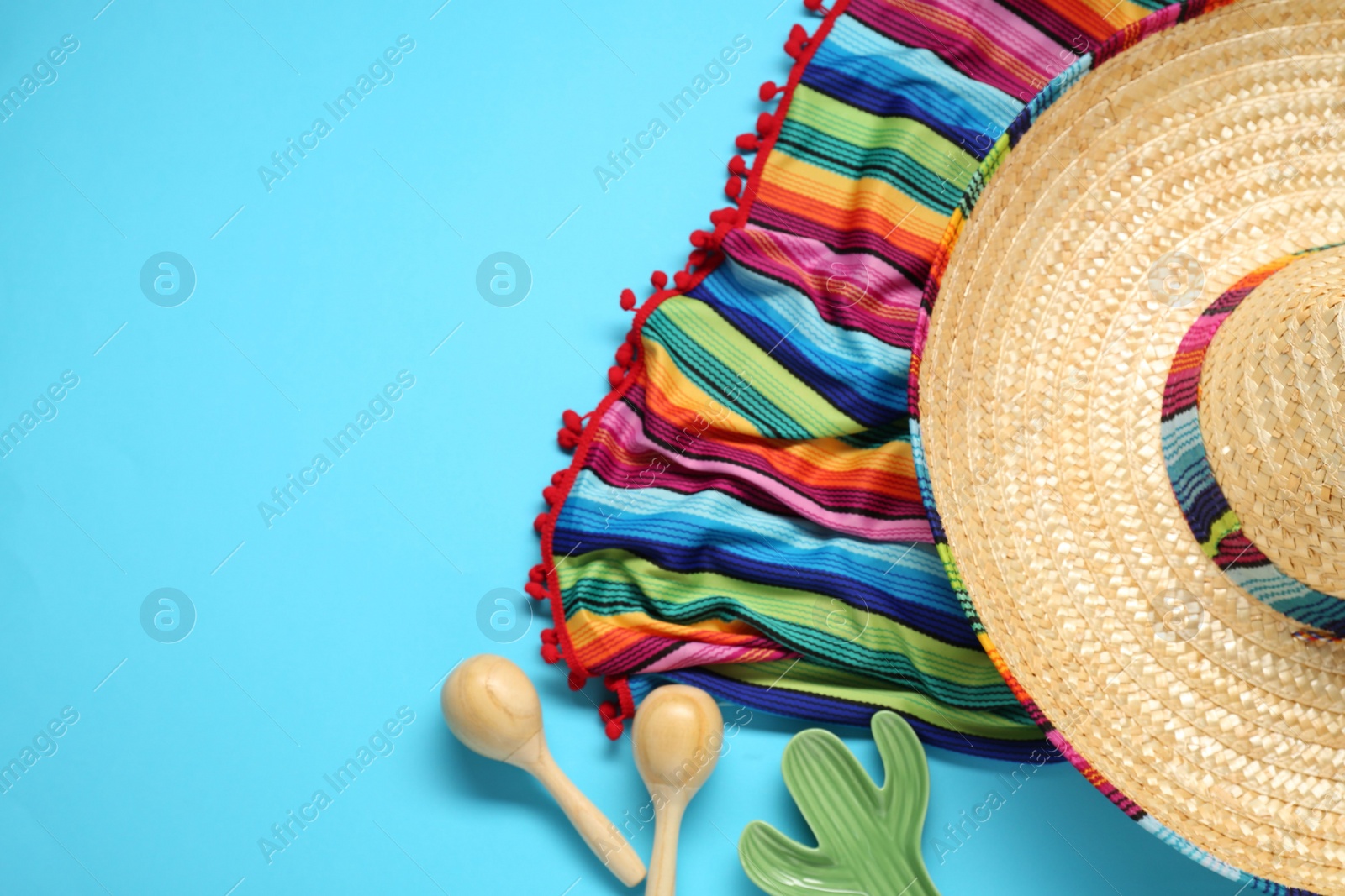 Photo of Mexican sombrero hat, maracas, toy cactus and colorful poncho on light blue background, flat lay. Space for text