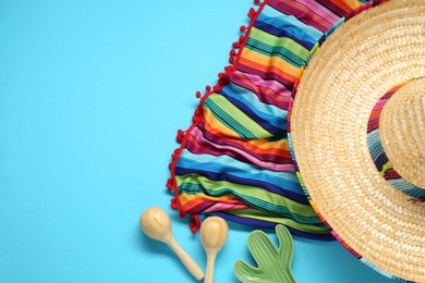 Mexican sombrero hat, maracas, toy cactus and colorful poncho on light blue background, flat lay. Space for text