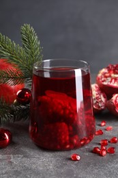 Aromatic Sangria drink in glass, Christmas decor and pomegranate grains on grey textured table, closeup