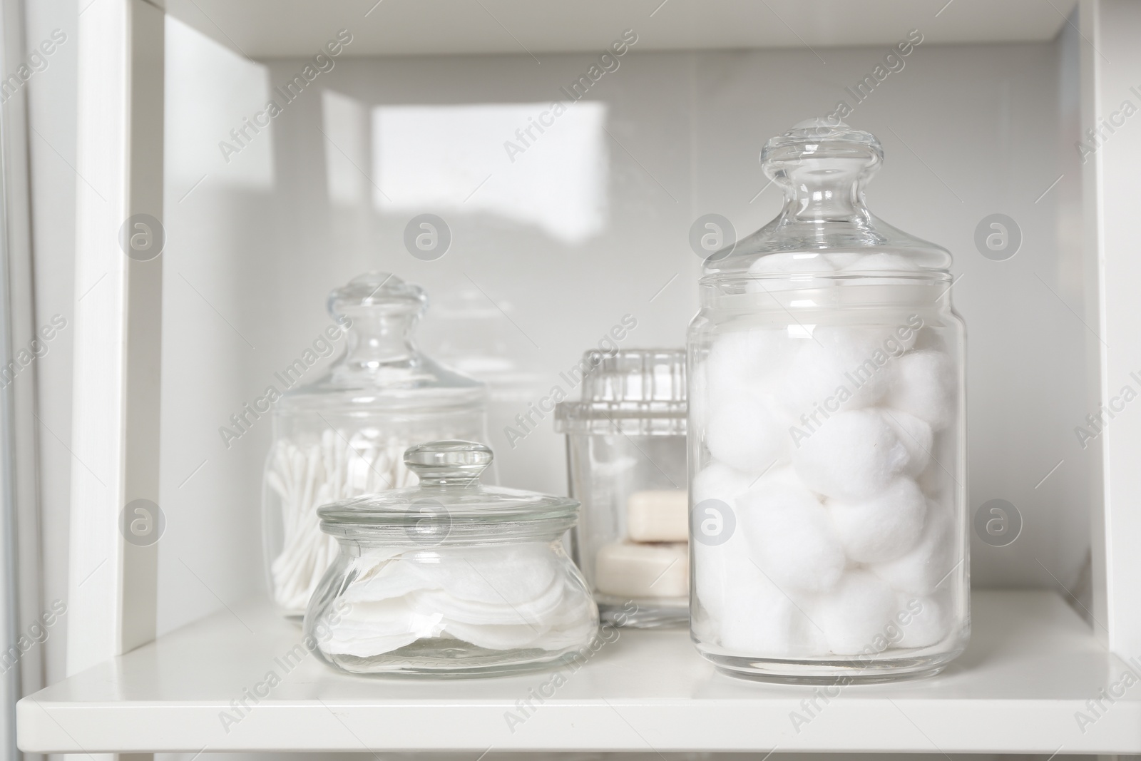 Photo of Cotton balls, swabs and pads on white shelf in bathroom