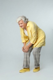 Full length portrait of senior woman having knee problems on grey background