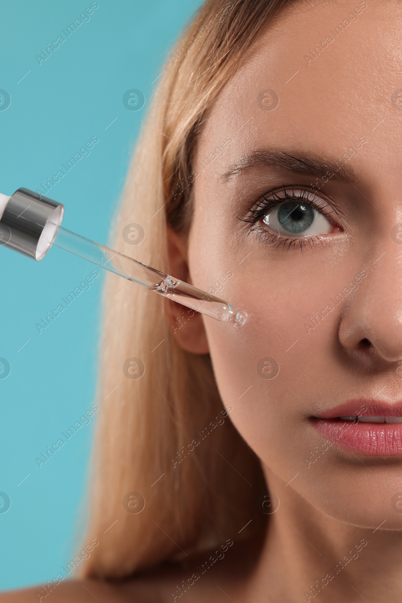 Photo of Beautiful woman applying cosmetic serum onto her face on light blue background, closeup