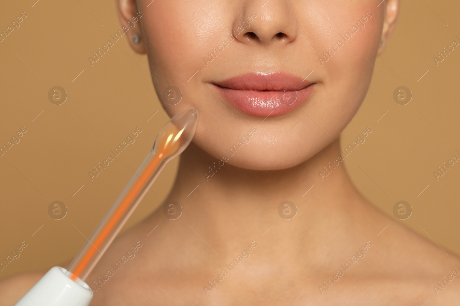 Photo of Woman using high frequency darsonval device on beige background, closeup