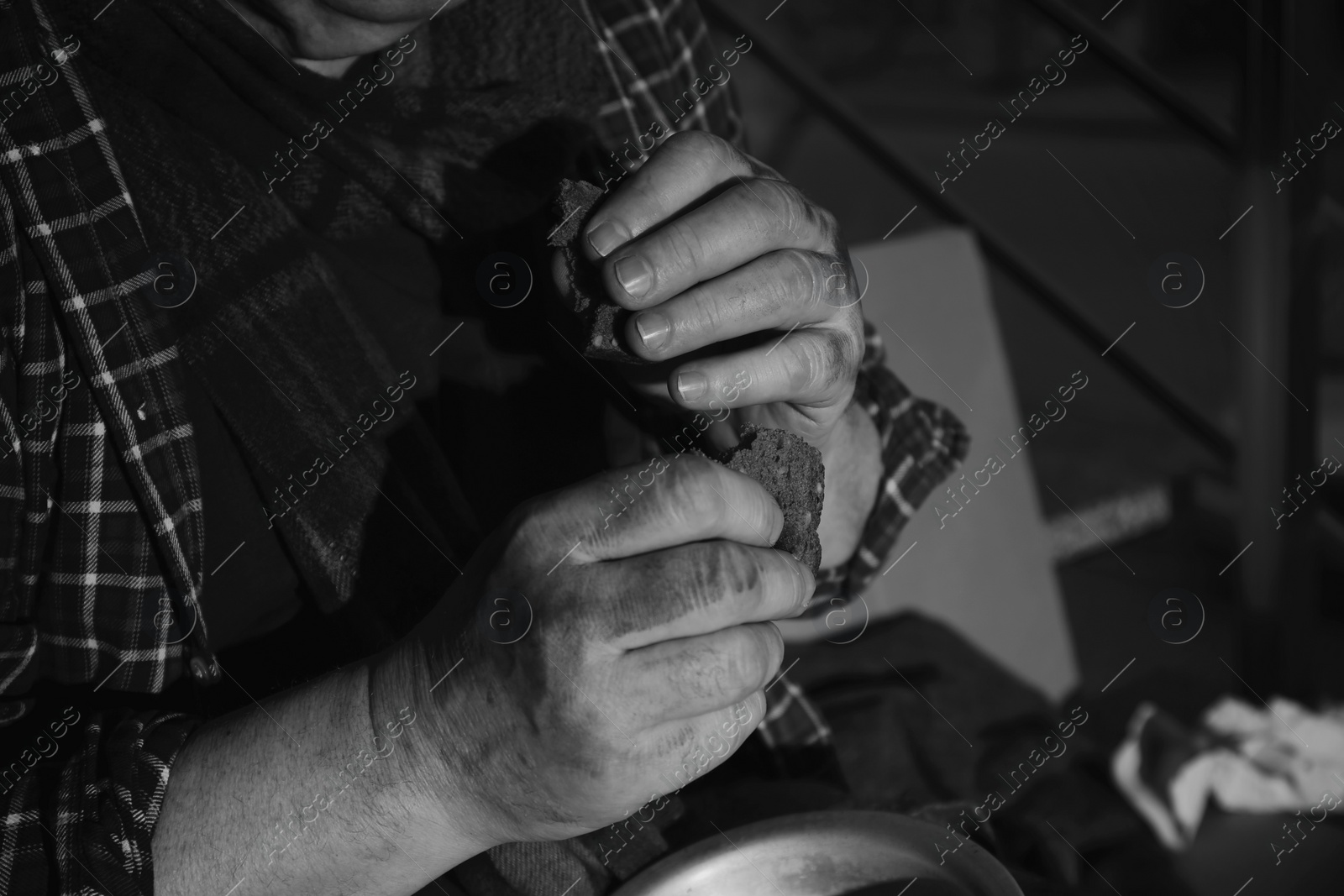 Photo of Poor senior man eating bread indoors, closeup. Black and white effect