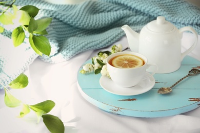 Photo of Wooden board with cup of lemon tea and teapot on fabric