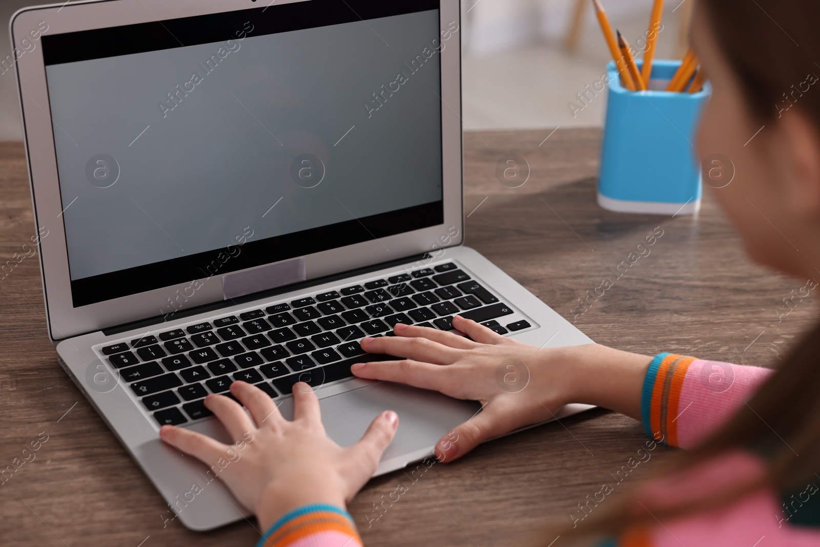 Photo of E-learning. Girl using laptop during online lesson at table indoors, closeup