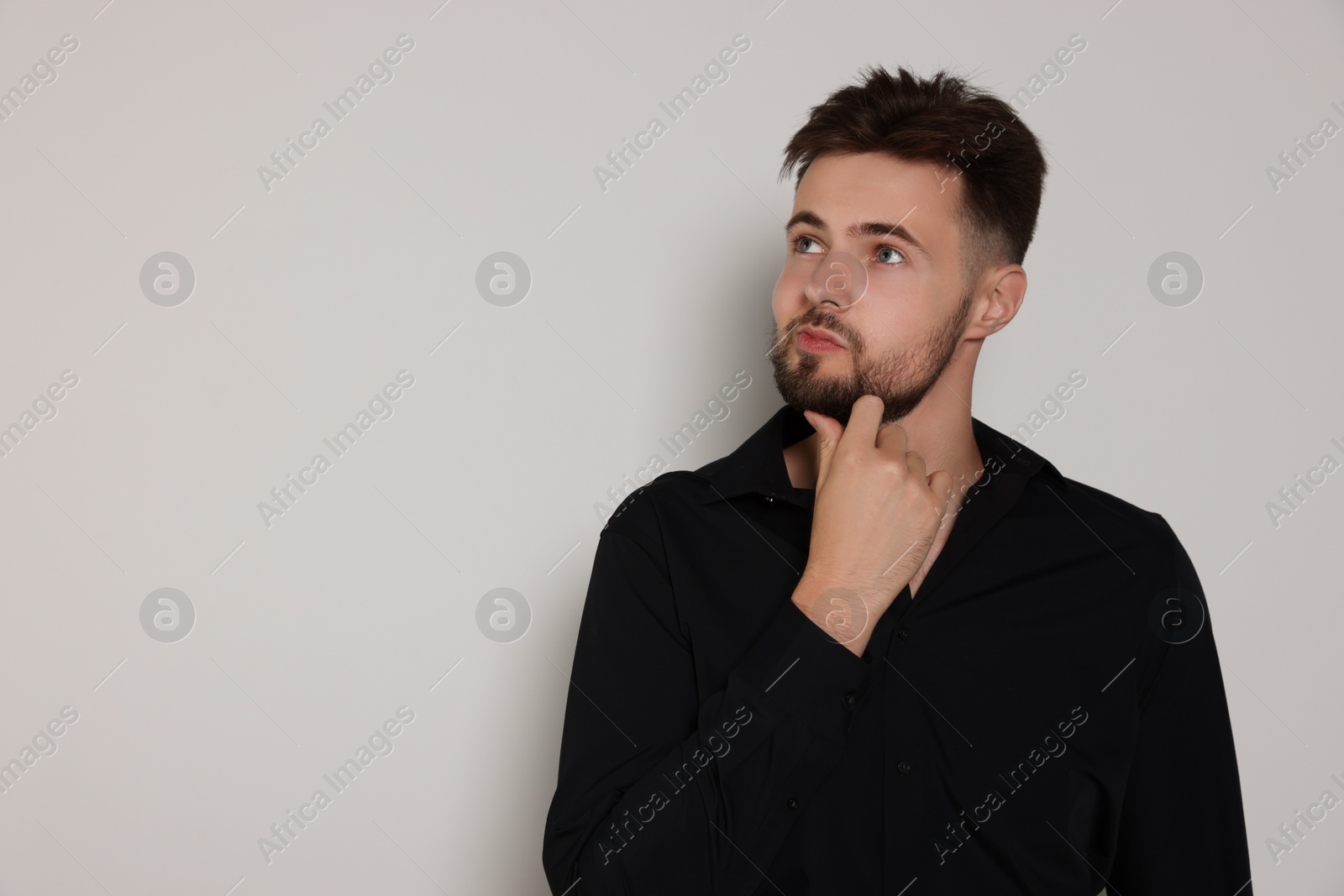 Photo of Thoughtful man in black shirt on light grey background, space for text