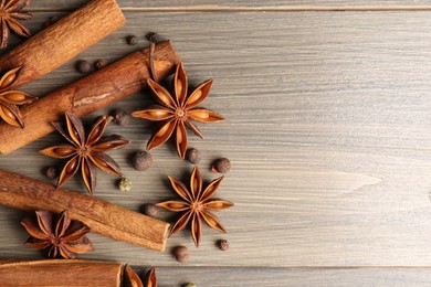 Aromatic anise stars, pepper and cinnamon sticks on wooden table, flat lay. Space for text