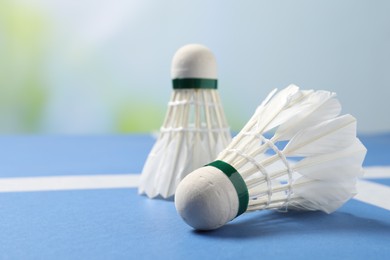 Feather badminton shuttlecocks on blue table against blurred background, closeup. Space for text