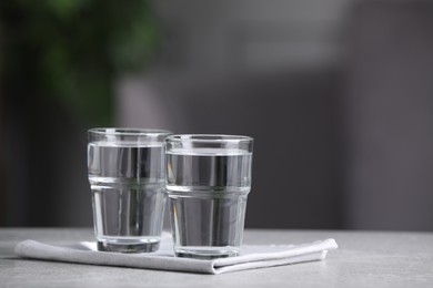 Photo of Glasses of clean water on light grey table indoors, space for text