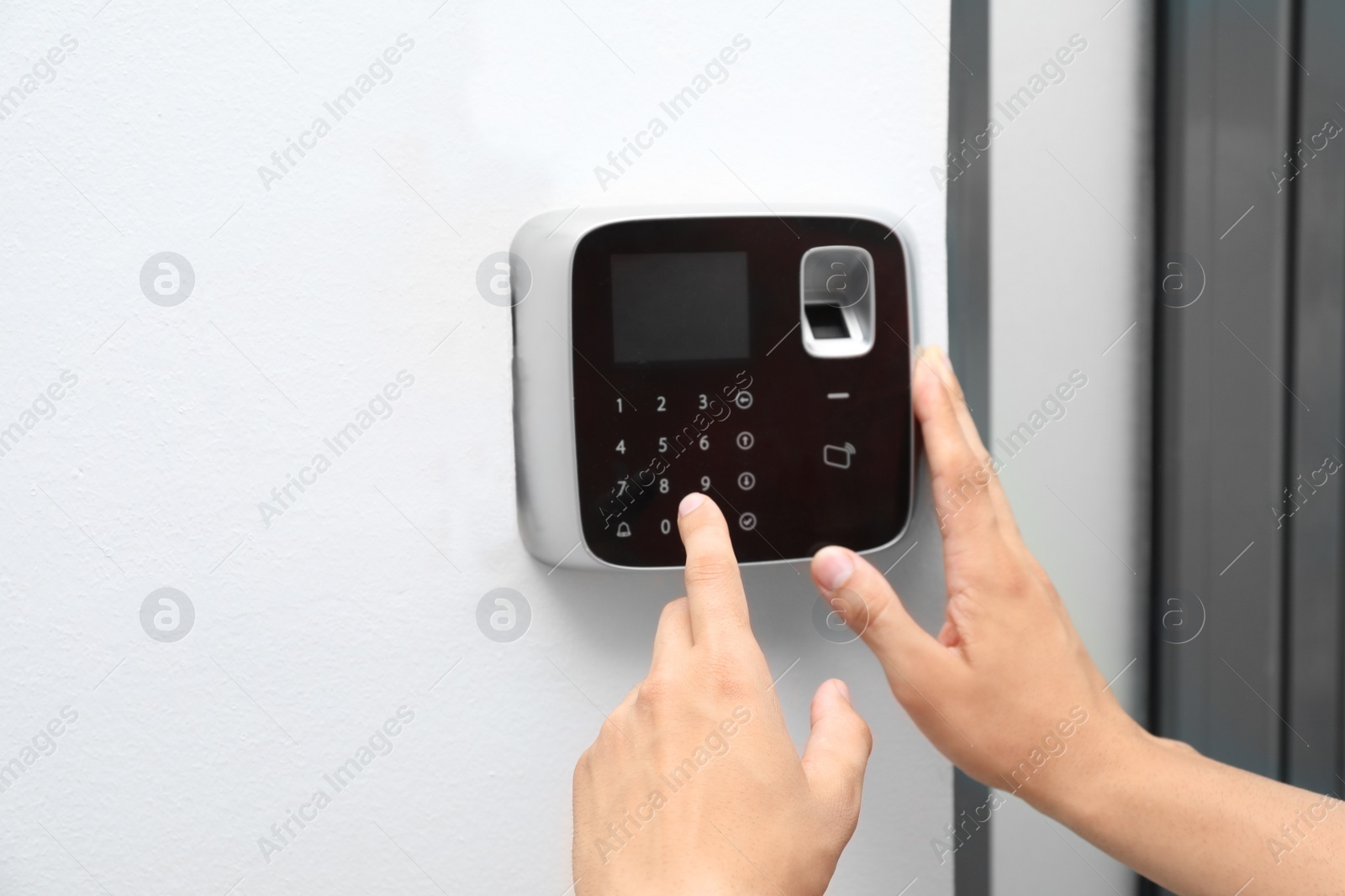 Photo of Young man entering code on alarm system keypad indoors