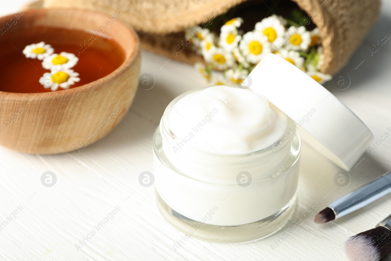 Photo of Jar of cream, brushes and chamomiles on white wooden table