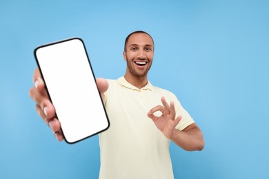 Photo of Young man showing smartphone in hand and OK gesture on light blue background