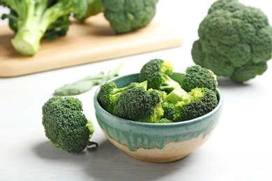 Photo of Bowl and fresh broccoli on light grey table