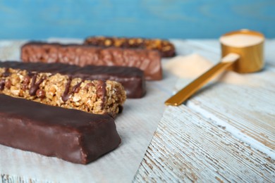 Photo of Different tasty bars and scoop of protein powder on wooden table, closeup