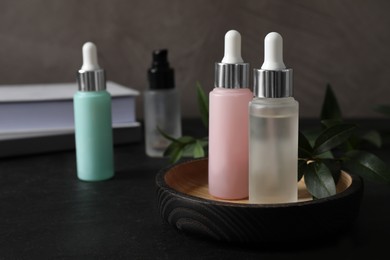 Bottles of serum on black table, space for text. Cosmetic products